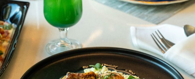 two dinner meals with a green cocktail on a white table cloth