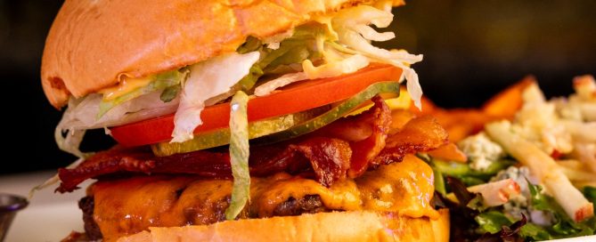 Close-up of a delicious burger topped with crispy bacon, lettuce, tomato, and cheese served on a white plate