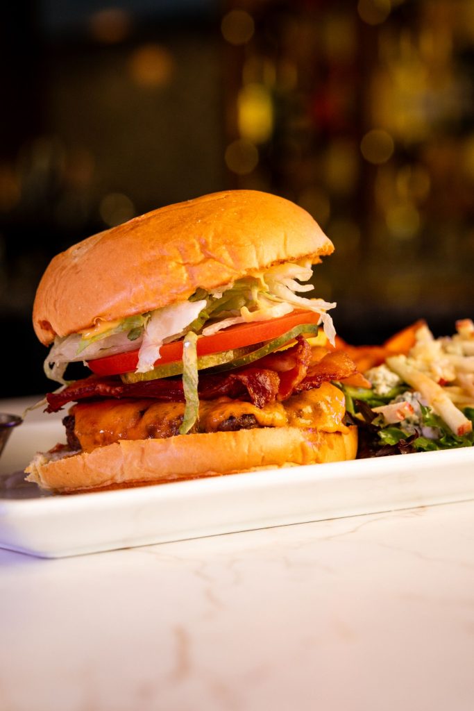 Close-up of a delicious burger topped with crispy bacon, lettuce, tomato, and cheese served on a white plate