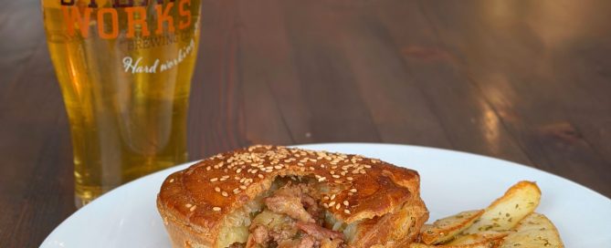 Meat pie and potato wedges on white plate with beer gralss