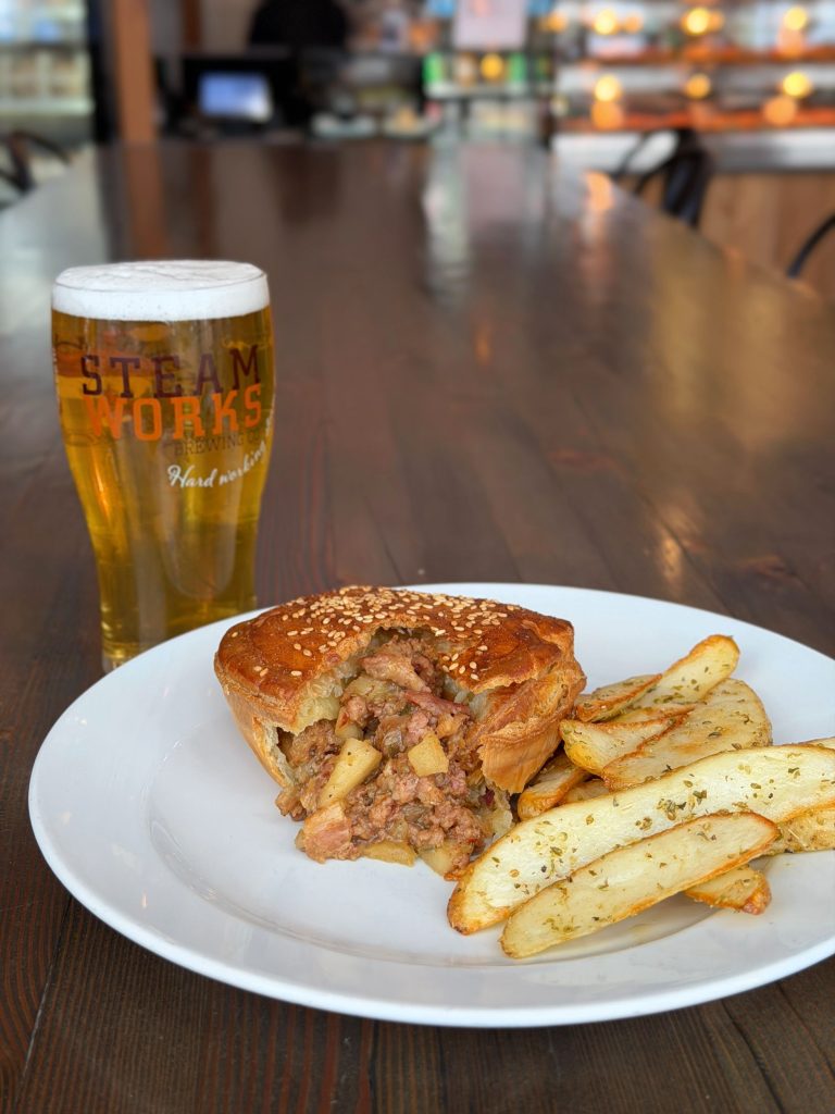Meat pie and potato wedges on white plate with beer gralss