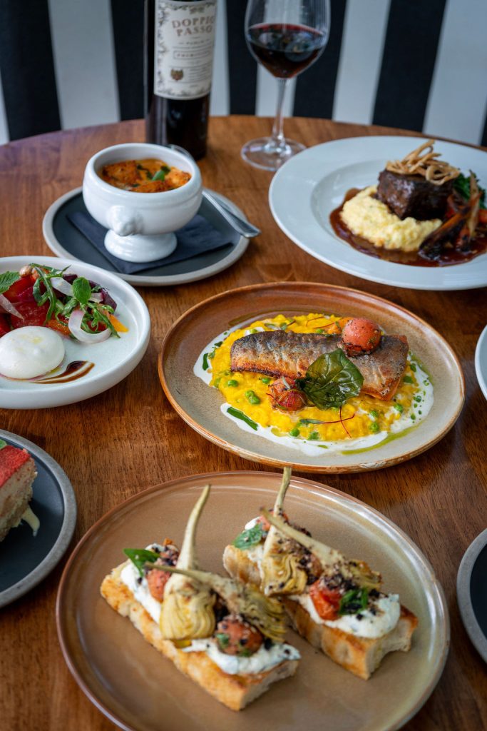 An array of colourful dishes with a bottle of red wine