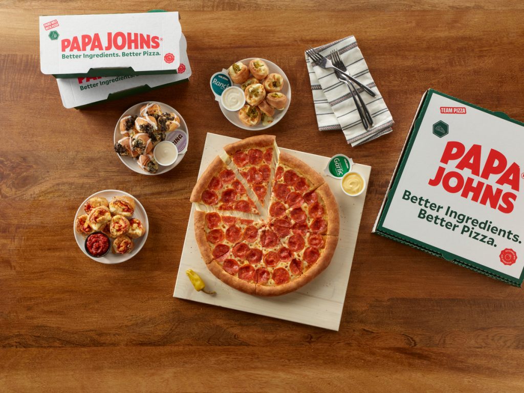 Papa Johns pepperoni pizza on top of pizza box surrounded by 3 appetizers in white dishes - Jalapeno bites, chicken parmesan bites, and oreo cookie bites