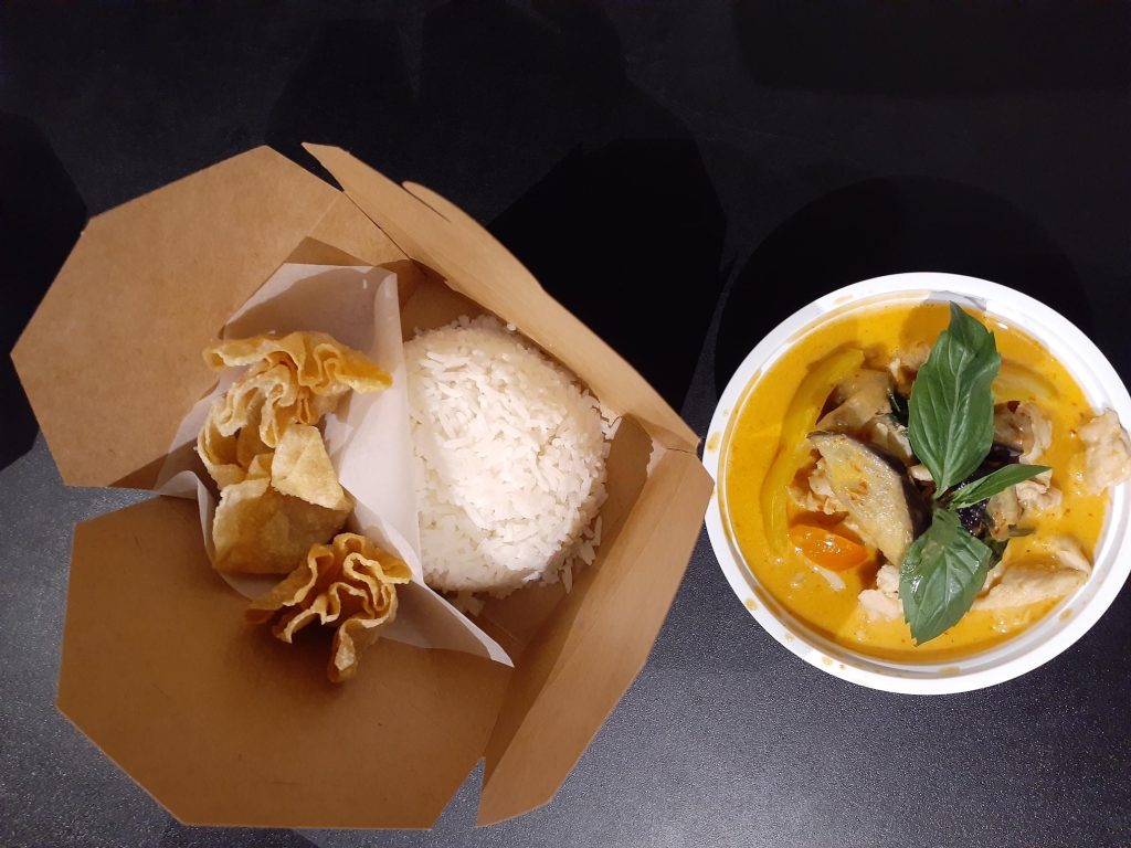 rice and crispy wontons in a to-go box and yellow curry and fresh basil in white to-go box